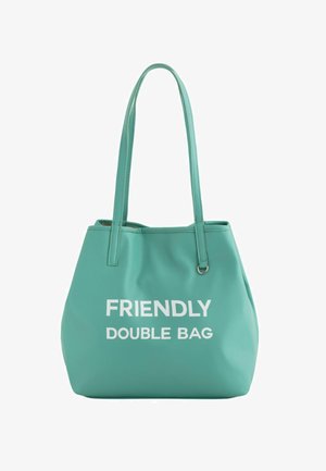 Turquoise synthetische draagtas met twee handvatten, met de tekst "VRIENDELIJKE Dubbele TAS" in vet witte letters op de voorkant.