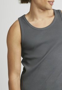 Débardeur gris côtelé avec un col rond. Le tissu semble lisse et doux. Le design sans manches met en valeur les épaules et les bras supérieurs.