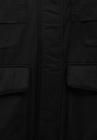 Giacca imbottita nera con una texture liscia, dotata di due grandi tasche frontali e una chiusura con zip nascosta lungo il centro.