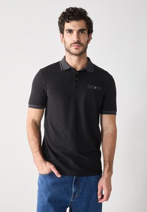 Čierna polo košeľa so šedým golierom a rukávmi, vybavená zapínaním na gombíky a náprsné vrecko s horizontálnym prúžkovaním. Džínsy.