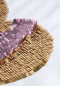 Flitteres minta arany és rózsaszín korongokkal fehér szövet hátterén, texturált felülettel és határozott színkontraszttal.