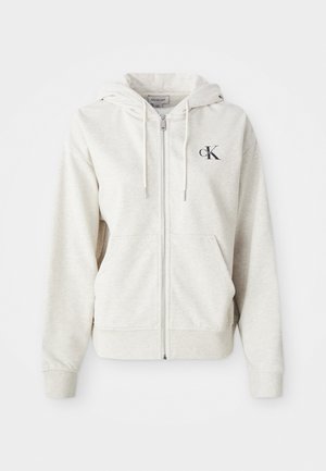 Lys grå zip-up hettegenser med snorhette, frontlommer og en liten brodert logo på brystet. Glatt tekstur. Materiale av bomullsblanding.
