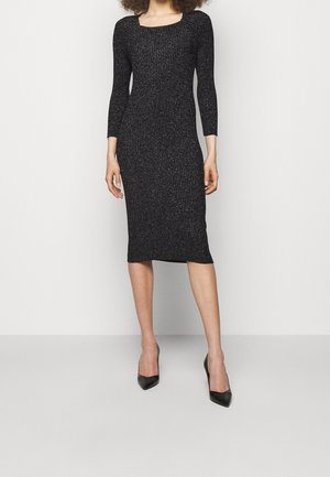 Vestido midi de punto acanalado negro con mangas a tres cuartos, con escote redondeado y un sutil brillo. Combinado con tacones altos negros.