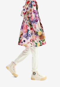 Imperméable à motif floral avec un design rose et multicolore, assorti à un pantalon blanc et des baskets montantes crème ornées d'un patch.