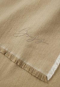 Beige cashmere tørklæde med frynser og subtil tekstur. Har broderet logo i lys brun. Glat, luksuriøst udseende.