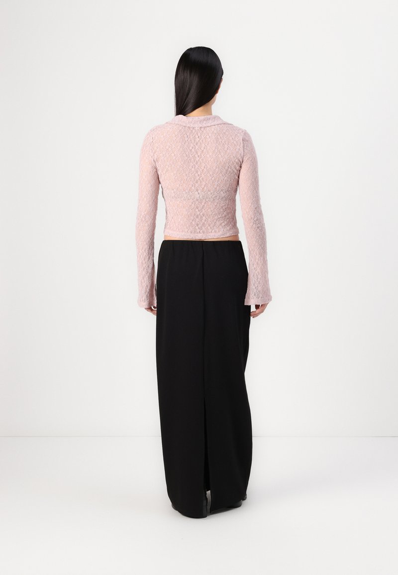 Top in pizzo rosa a maniche lunghe con design corto, dotato di colletto, abbinato a una gonna nera lunga fino al pavimento.
