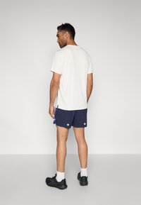 Λευκό κοντομάνικο μπλουζάκι συνδυασμένο με ναυτικά σορτς που διαθέτουν λευκές λεπτομέρειες. Μαύρα αθλητικά παπούτσια και εμφανείς λευκές κάλτσες ολοκληρώνουν την εμφάνιση.