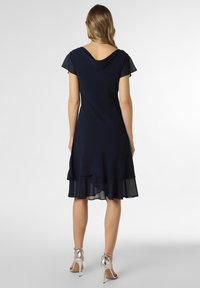 Navy dress with short cap sleeves, a low back, and a layered ruffle hem. Paired with silver high-heeled sandals.