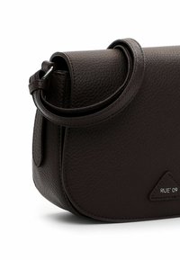 Dark brown leather shoulder bag with a curved shape, featuring a textured finish and a triangular logo detail. Adjustable strap included.