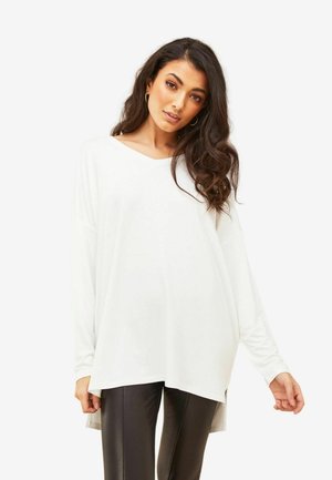 Haut blanc à manches longues avec décolleté en V et coupe décontractée, doté d'une fente sur les côtés. Assorti à un pantalon noir ajusté.