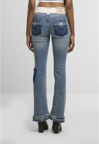 Jean en denim évasé de couleur bleu clair avec un ourlet effiloché. Équipé de poches arrière avec des coutures contrastées et une étiquette de marque à la taille.