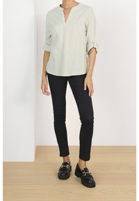 Light green striped blouse with a V-neck, rolled sleeves, paired with black skinny jeans and black loafers with a gold accent.