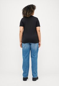 Μαύρο κοντομάνικο t-shirt, εφαρμοστό στη μέση, συνδυασμένο με ανοιχτό μπλε τζιν με ίσια γραμμή. Το μοντέλο απεικονίζεται από πίσω.