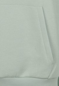 Lys grønn sweatshirt-stoff med en myk tekstur, med en kengurulomme og ribbede mansjetter i nederkant.