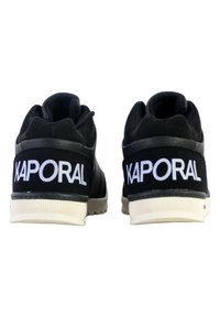 Zapatillas negras con una parte superior texturizada, que presentan un prominente logotipo blanco "KAPORAL" en el talón y una suela blanca en contraste.