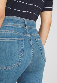 Džíny s vysokým pasem z modrého denimu s vybledlým povrchem, vybavené dvěma zadními kapsami a kontrastním šitím podél švů.