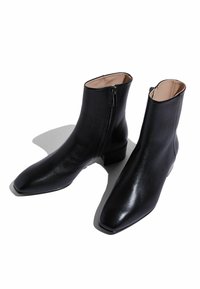Botas de cuero negras hasta el tobillo con punta afilada, cierre de cremallera y tacón bajo cuadrado. Textura suave con forro interior beige.
