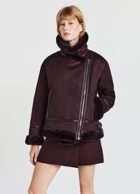 Giubbotto in shearling borgogna con colletto alto, chiusura con zip e rifiniture in pelliccia morbida. Presenta una finitura liscia e un design sportivo con tasche laterali.