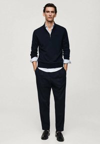 Navy zippered pullover sweater over a white collared shirt, paired with dark tailored pants and black leather loafers. Smooth texture.