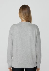 Sudadera gris claro de corte relajado, con cuello acanalado y mangas largas. Textura suave y aberturas laterales en el dobladillo, sin patrones visibles.
