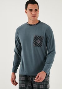 Hosszú ujjú, türkiz színű póló kerek nyakkivágással, szürke és fekete kockás zsebbel. Kockás nadrággal párosítva hasonló színekben.