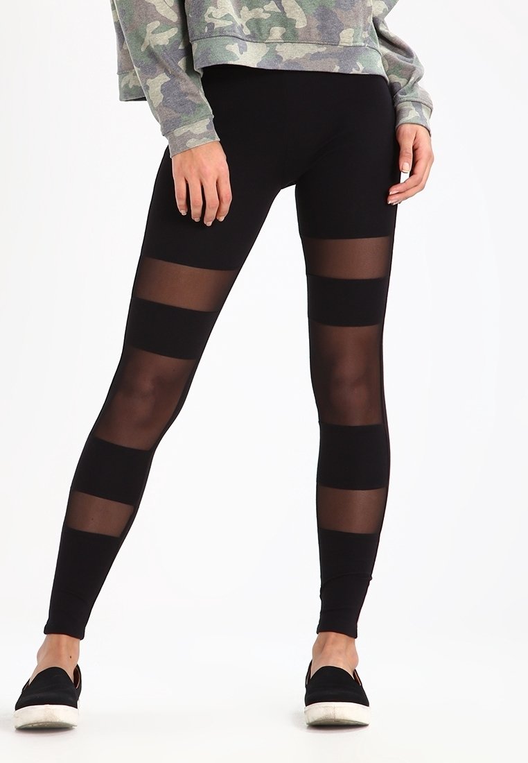 Leggings noirs avec des panneaux rayés transparents. Texture lisse avec un design ajusté. Associés à un sweat-shirt camouflage et à des chaussures noires à enfiler.