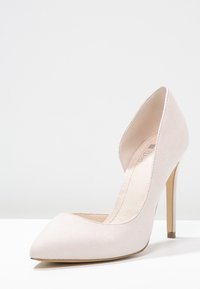 Ljusrosa mocka högklackad pumpsko med spetsig tå och en öppen sidodesign, med en tunn guldklack. Sömmen är slät med minimal detaljering.