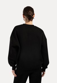 Černá oversized mikina s dlouhými rukávy, žebrovaným kulatým výstřihem a měkkou strukturou. Obsahuje uvolněný střih a minimalistický design.