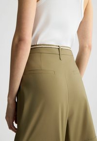 Pantaloni corti verde oliva con una consistenza liscia, caratterizzati da una cintura intrecciata bianca e due tasche posteriori. Il design include una chiusura a gancio e occhiello.