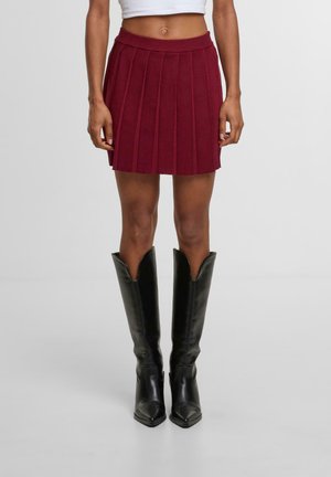Bordeaux plissé minirok met een rekbare tailleband, gecombineerd met zwarte kniehoge laarzen met een spitse neus in soepel leer.