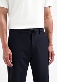 Donkerblauwe broek van een gladde, lichte stof, met een trekkoord in de taille en zijzakken, gepresenteerd met een wit shirt.