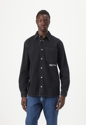 Črna denim srajca z gumbom na zapiranju, enojno prsno žepem in vezenim logotipom. Ima klasičen ovratnik in dolge rokave.