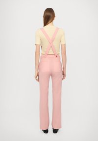 Pink trousers with suspenders, high-waisted design, straight leg, paired with a fitted light beige top. Smooth fabric, minimal detailing.