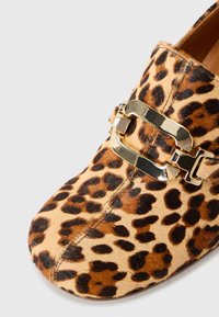 Leopardų rašto slip-on batai su auksinės spalvos metaliniu užsegimu. Turi tekstūruotą plaukuotą paviršių ir apvalų pirštą.