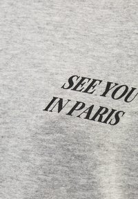 Szary bawełnowy t-shirt o miękkiej teksturze z czarnym nadrukiem: "DO ZOBACZENIA W PARYŻU." Prosty i nowoczesny design bez dodatkowych grafik.