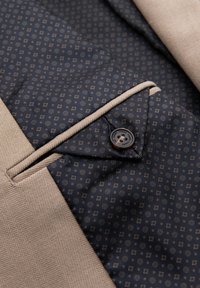 Tissu beige en chevrons contrastant avec un tissu foncé à motifs, avec un bouton et un passepoil beige.
