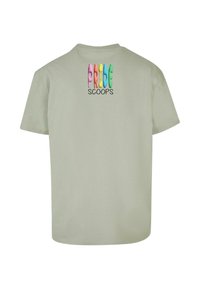 Lys grøn t-shirt i bomuld med korte ærmer. Teksten på ryggen viser "PRIDE" i flerfarvede bogstaver og "SCOOPS" i sort.