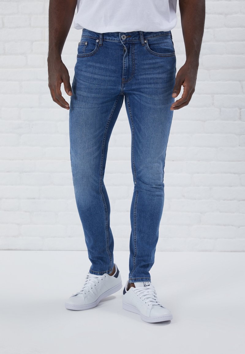 Blå denimjeans med slim fit, med en medelhög midja, fem fickor och subtila blekningar. Bärs med vita sneakers.