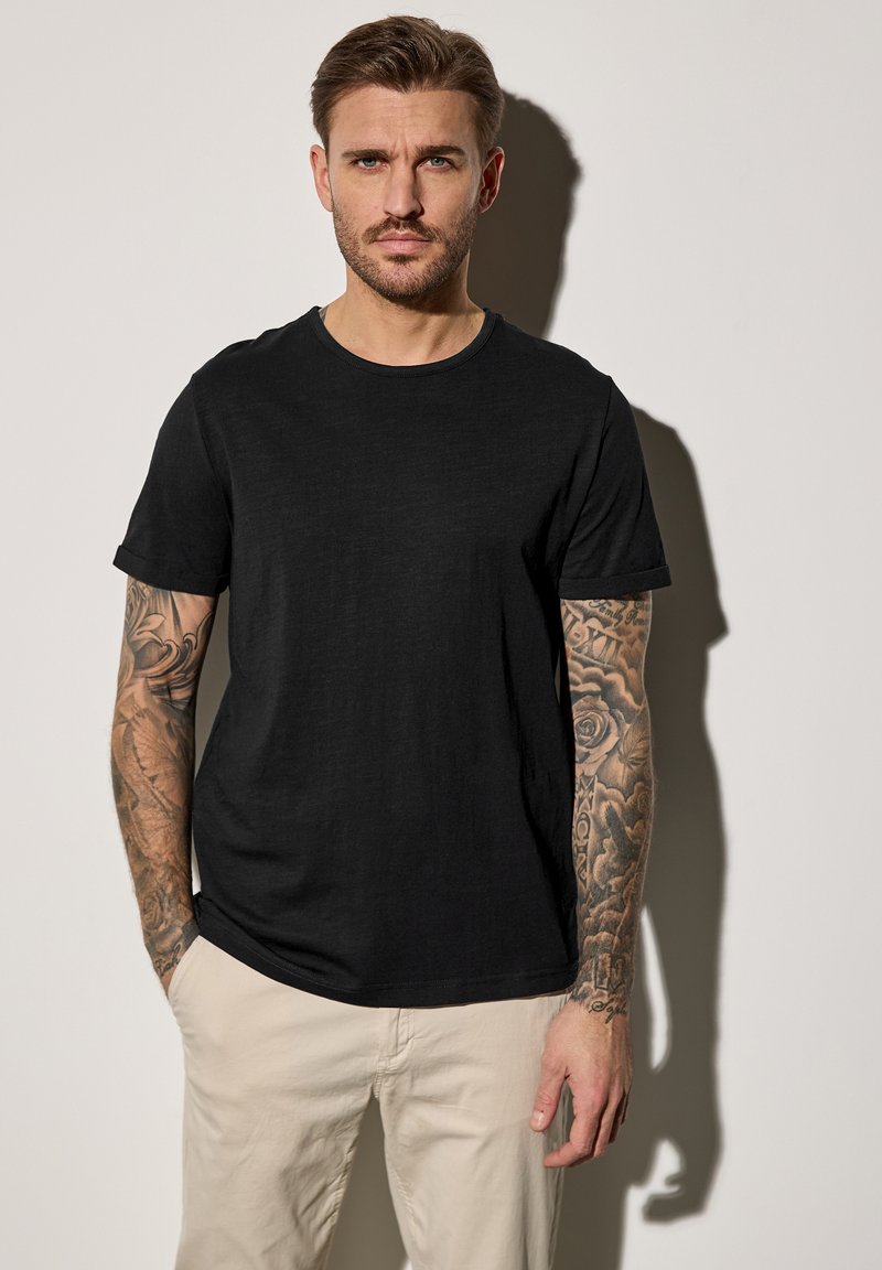 Camiseta negra de cuello redondo hecha de tela suave, con mangas cortas y un corte relajado, combinada con pantalones de color claro.