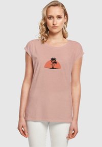 Lys pink kortærmet T-shirt med rund hals, der har en sort palmetræsilhuet mod en orange solnedgangs grafik.