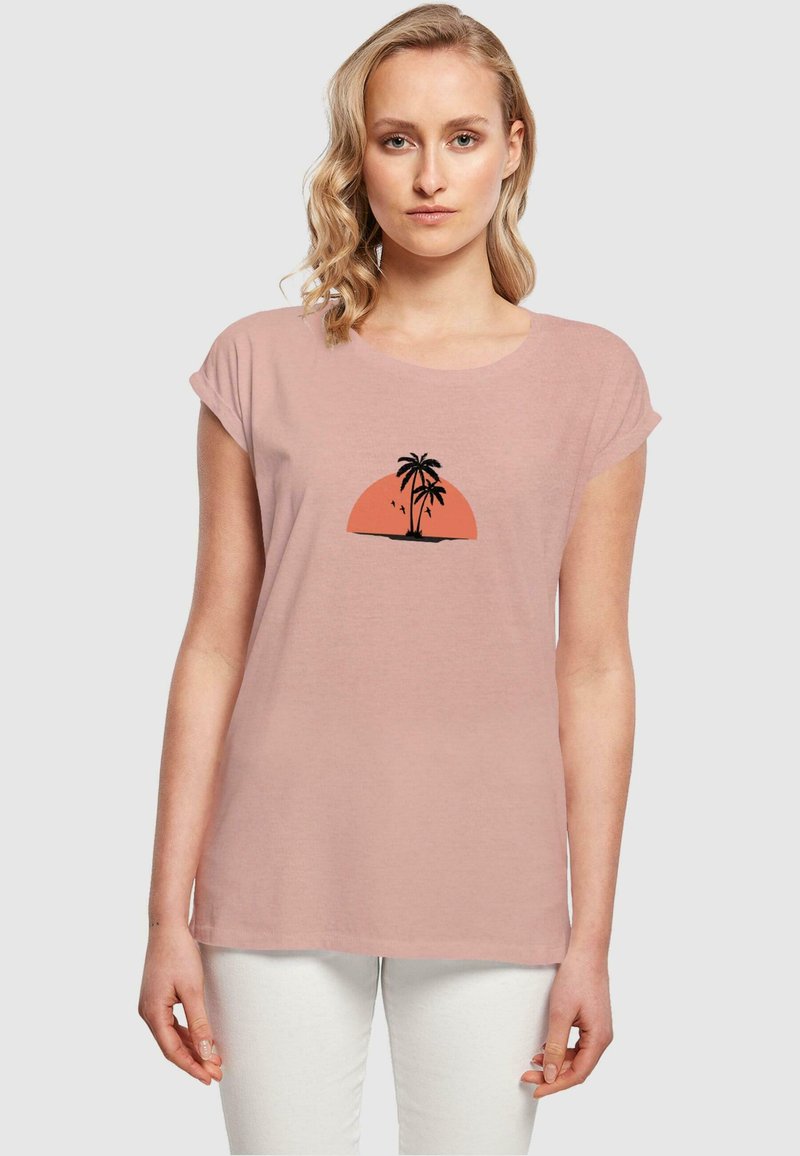 Lys pink kortærmet T-shirt med rund hals, der har en sort palmetræsilhuet mod en orange solnedgangs grafik.