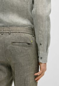 Camicia di lino grigia con polsini bottonati, abbinata a pantaloni di lino grigi chiari con tasca posteriore e dettagli di cucitura.
