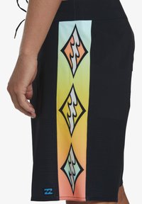 Pantaloni corti neri con un pannello laterale a gradiente che presenta motivi di diamanti e onde in arancione, giallo e azzurro chiaro. Finitura testurizzata.