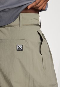 Bermudas verde-claro feitas de tecido leve, com um bolso traseiro com um logótipo em preto e branco e uma superfície texturada.