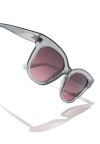 Ochelari de soare gri supradimensionați cu lentile roz închis și rame transparente. Prezintă o formă curbată tip „ochi de pisică” și un logo proeminent pe braț.