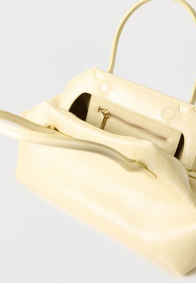 Μαλακή κίτρινη δερμάτινη τσάντα χειρός με ανοιχτό καπάκι, που αποκαλύπτει εσωτερική τσέπη με φερμουάρ και χρυσό τράβηγμα φερμουάρ.