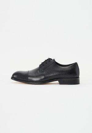Chaussure habillée pour homme en cuir noir avec bout droit, lacets et petit talon empilé sur fond blanc.