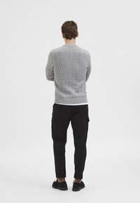 Szürke, kerek nyakú, kötött pulóver hátulnézetből, fekete cargos nadrággal párosítva, bordázott mandzsettákkal és szegéllyel.