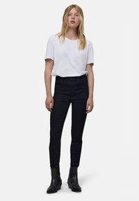 Biała bawełniana koszulka w połączeniu z czarnymi, obcisłymi jeansami z wysokim stanem i czarnymi botkami za kostkę. Prosty krój, dopasowana sylwetka i jednolite kolory.