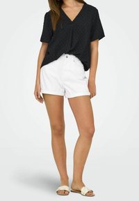 Black short-sleeve top with a V-neck and textured pattern, paired with white denim shorts featuring a rolled hem and front pockets.